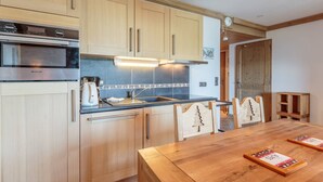 A modern kitchen with wooden cabinets, a Brandt oven, a coffee maker, and a dining table with wooden chairs. - Ski-in/ski-out apartment, 2 bedrooms, covered parking included (Les Arcs 1800)