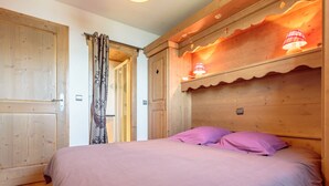 A bedroom with a wooden headboard, a bed with pink bedding, and a door with a curtain. - Ski-in/ski-out apartment, 2 bedrooms, covered parking included (Les Arcs 1800)