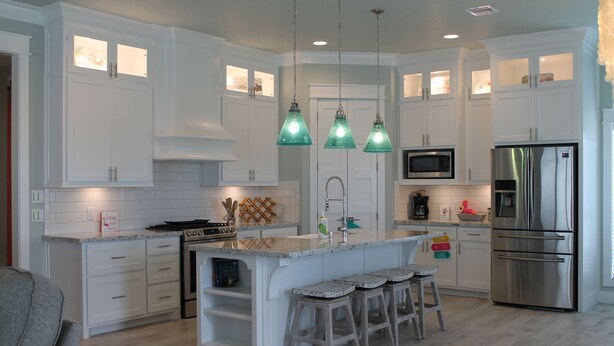 A spacious kitchen with white cabinetry, a central island with bar stools, stainless steel appliances, and pendant lighting.