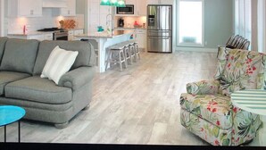 A modern kitchen with white cabinets, a stainless steel refrigerator, and a dining area with a floral sofa and a round table.