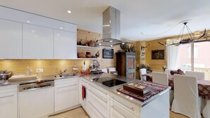 Una cocina moderna con armarios blancos, una isla central con estufa y una zona de comedor con mesa y sillas.