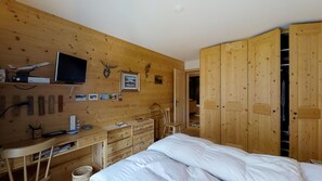 A bedroom with a wooden wall, a bed, a desk, a chair, and a wardrobe.