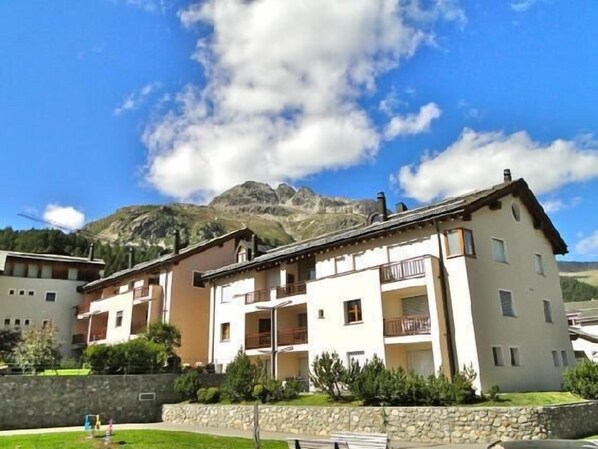 A multi-story building with balconies, set against a mountainous backdrop.