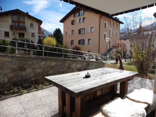 An outdoor wooden table with a remote control, set against a stone wall and a clear sky.