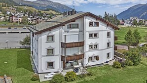 A multi-story residential building with a balcony, surrounded by greenery and mountains. - 3-room apartment on the ground floor, about 90 m2. (Celerina/Schlarigna)