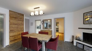A dining area with a wooden table and red chairs, a wooden accent wall, a mirror, and a fireplace.