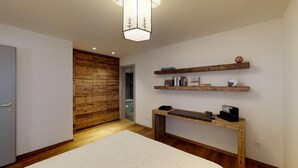A modern bedroom with a wooden floor, a white bed, a wooden console table with books, and a wooden wall panel. - 3-room apartment on the ground floor, about 90 m2. (Celerina/Schlarigna)