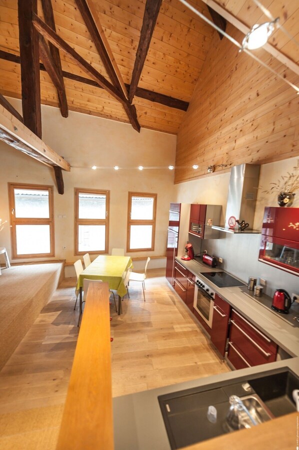 A spacious kitchen with wooden beams, a dining area with a long table, and a view through large windows. - Magnificent apartment, 656 feet from the lake of Annecy (Duingt)