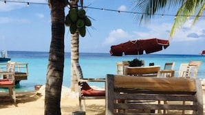 Ein Essbereich am Strand mit einem Holzstuhl, einem Teller mit Dessertresten und Blick aufs Meer.