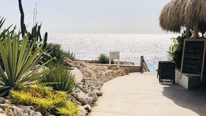 Ein Weg führt zu einem Strand, an dem ein Schild 'Beach House' und eine Speisekarte zu sehen sind.