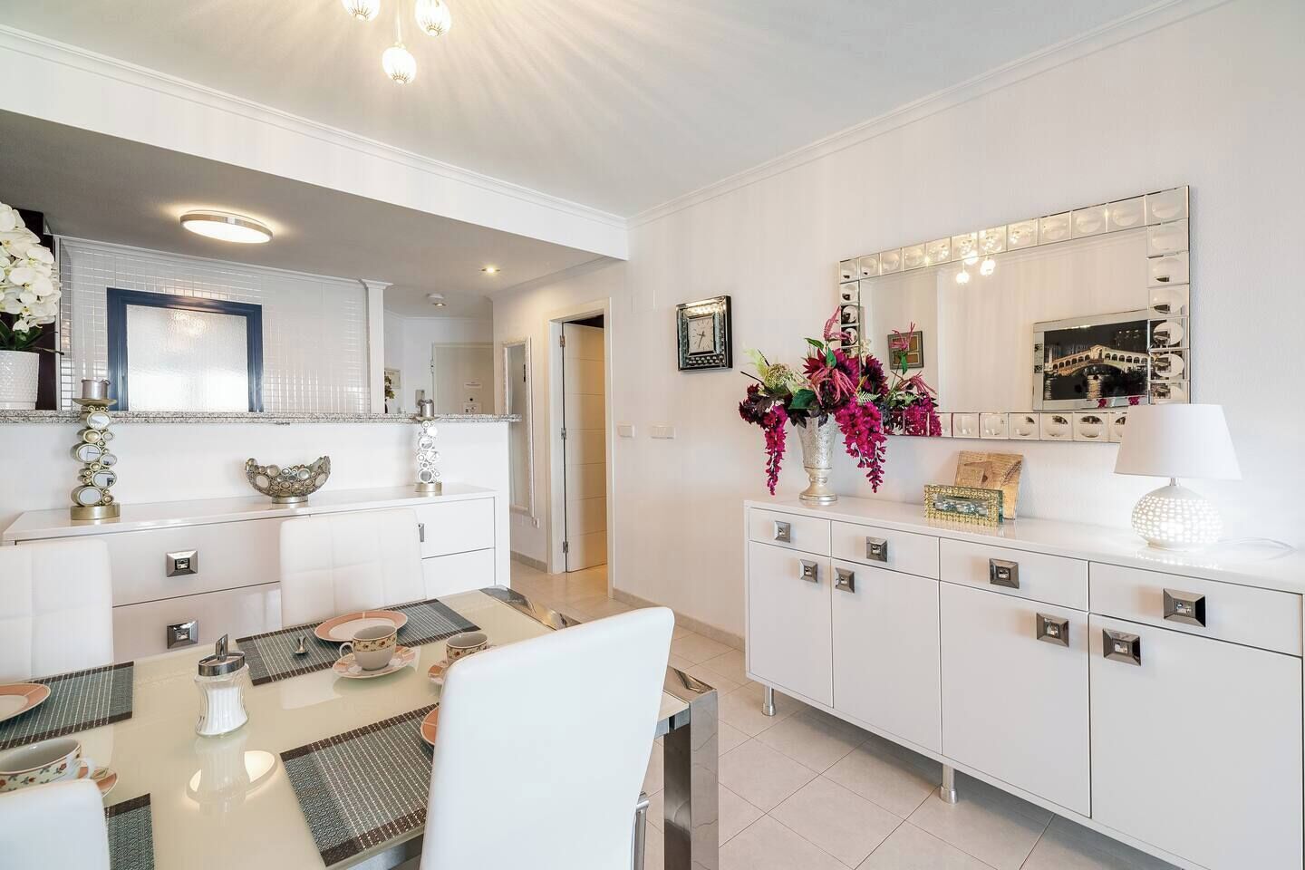 Una cocina moderna con armarios blancos, una mesa de comedor y un espejo grande sobre la encimera.