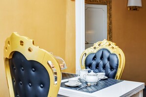 Une table à manger recouverte d’une nappe blanche, une chaise noire et dorée, et un miroir encadré de doré.