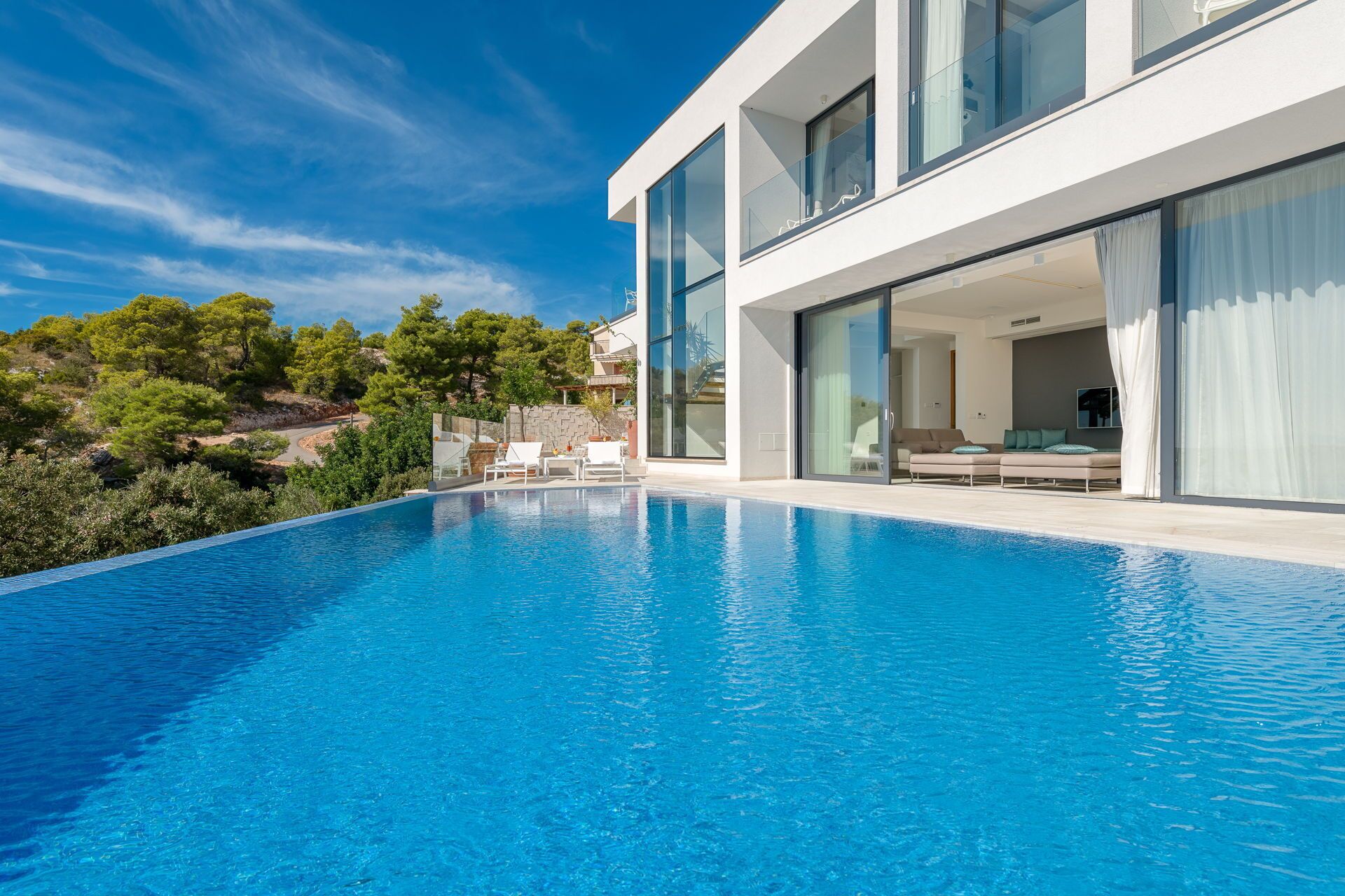 Une maison moderne dotée d’une piscine, de grandes fenêtres et offrant une vue sur les arbres.