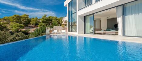 Une maison moderne dotée d’une piscine, de grandes fenêtres et offrant une vue sur les arbres.