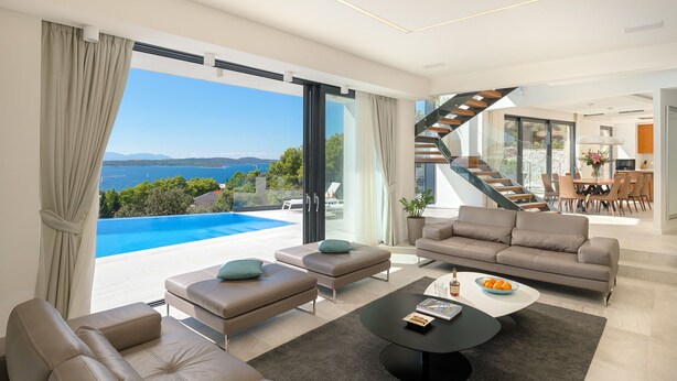 Ein modernes Wohnzimmer mit großem Fenster mit Blick auf Pool und Meer, einer Treppe und einem Essbereich.