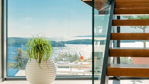 Ein weißer Topf mit Pflanze auf einem Balkon mit Blick auf das Meer und die Berge.