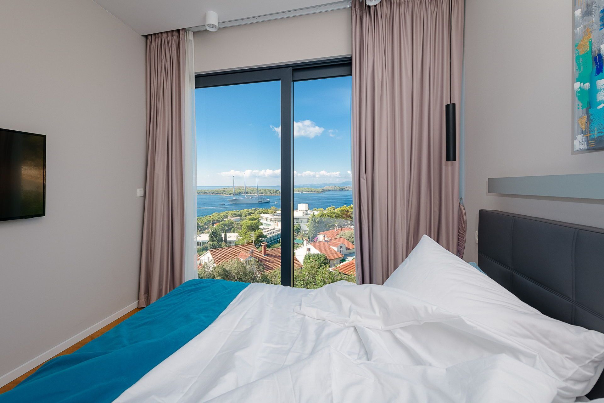 A bedroom with a bed, a view of a bridge and water, and a painting on the wall.