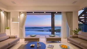 Ein modernes Wohnzimmer mit zwei Sofas, einem Couchtisch und Blick auf das Meer bei Sonnenuntergang.