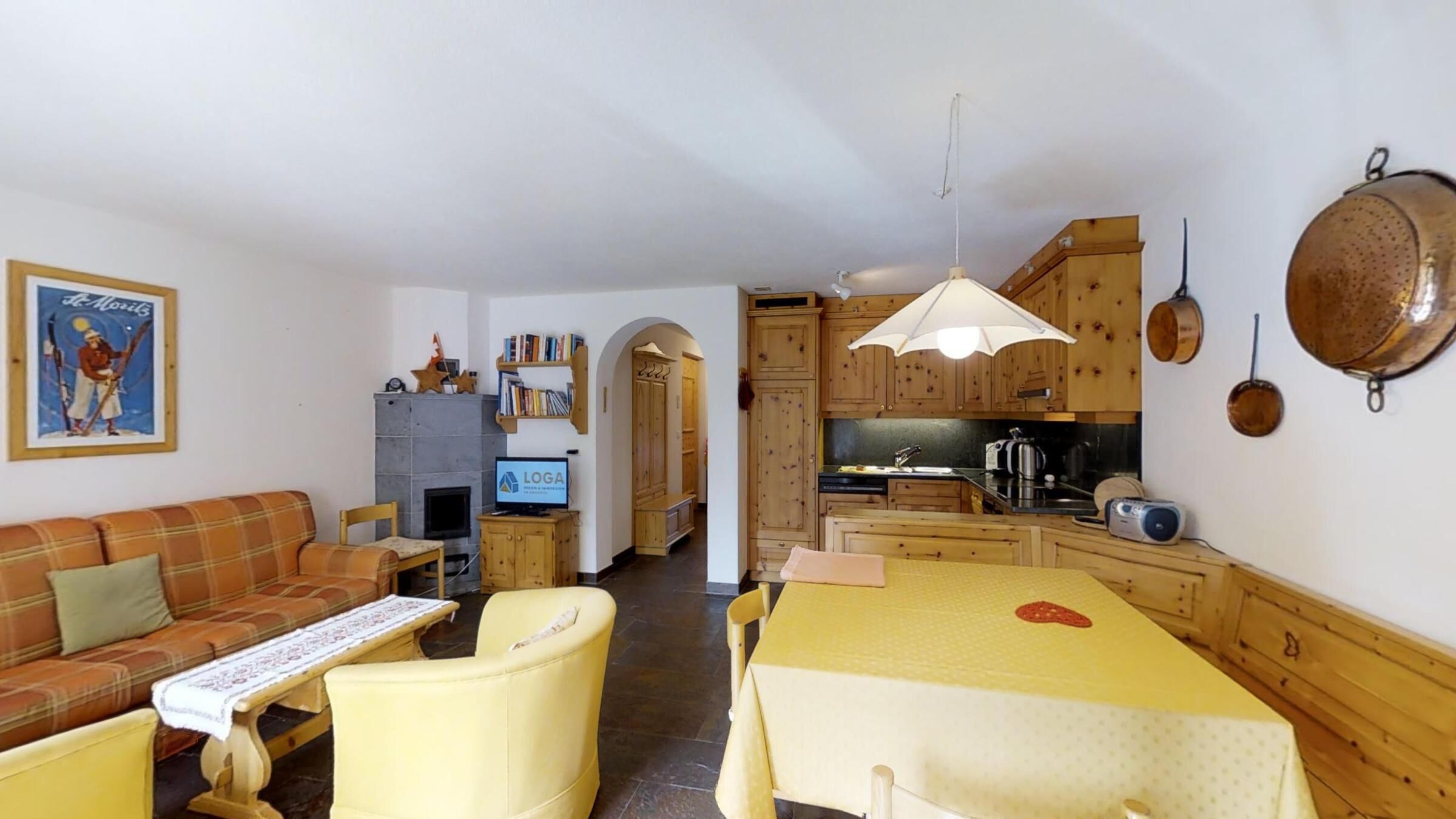 Een gezellige woonkamer met een bank, een tafel en een televisie. Er is een keuken met houten kasten en een eettafel.