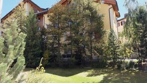 Un immeuble à plusieurs étages, doté d’un toit en pente, entouré d’arbres denses et d’une zone herbeuse.