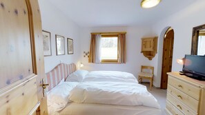 Une chambre à coucher comprenant un lit, une commode, une chaise, une fenêtre avec des rideaux et des tableaux accrochés au mur.