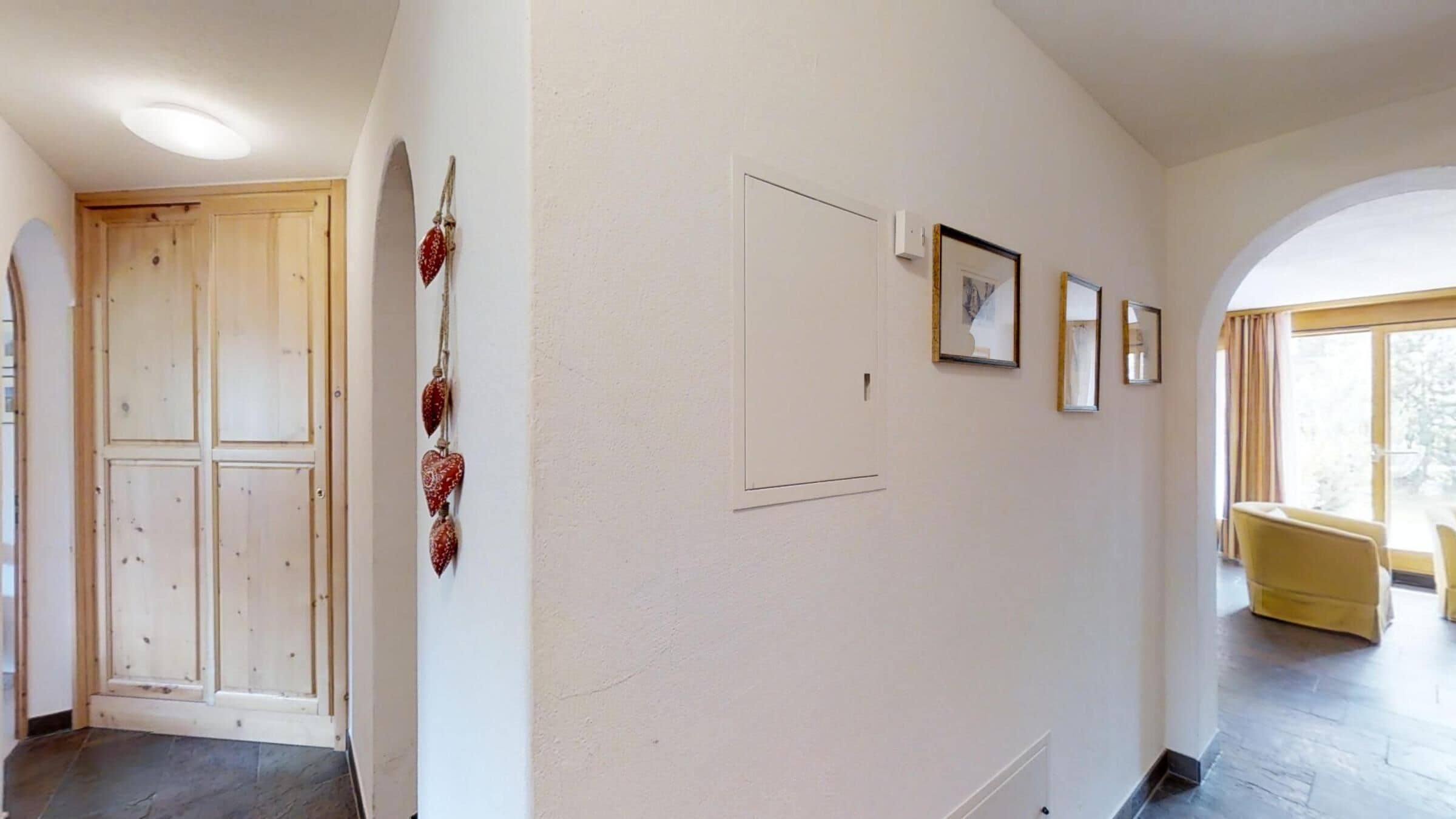 A hallway with a wooden door, a wall-mounted decoration, and framed pictures.