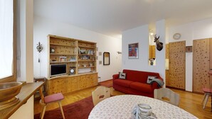 Ein gemütliches Wohnzimmer mit einem roten Sofa, Holzböden, einem Fernseher und einem Esstisch mit Blumenmuster-Tischdecke.