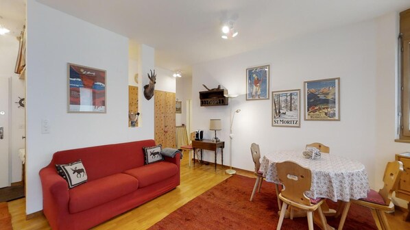 A cozy living room with a red sofa, a wooden dining table with chairs, and various wall decorations including a moose head and framed pictures.