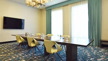 Un salón de conferencias con una mesa grande, sillas amarillas, un televisor de pantalla plana y una alfombra estampada.