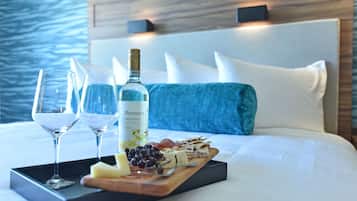 Una cama con cabecera de madera, una bandeja con vino, copas y una tabla de quesos.
