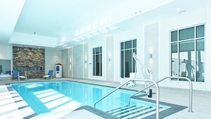 Una piscina interior moderna con marcas claras para carriles, una pared de acento de piedra y una escalera que conduce al área de la piscina.