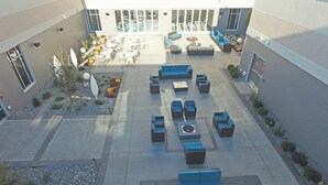 Un patio al aire libre con varios arreglos de asientos, incluyendo sofás y sillones, rodeado de un jardín con diversas plantas y flores.