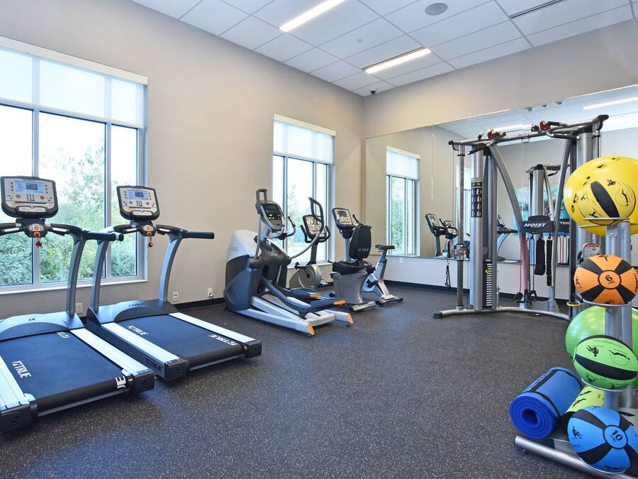 A gym with treadmills, elliptical machines, a weightlifting area, and exercise balls.