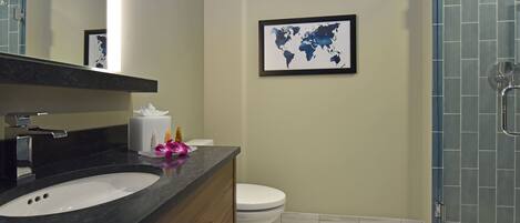 Un baño moderno con lavamanos de mármol, inodoro, un mapa mundial enmarcado y una cabina de ducha de vidrio.