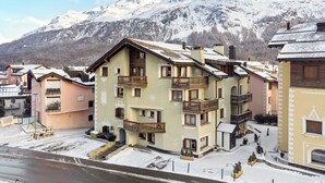 A multi-story building with balconies, a snow-covered street, and mountains in the background.