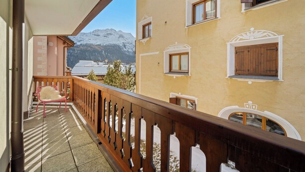 A balcony with a wooden railing, a chair, and a view of snow-covered mountains.