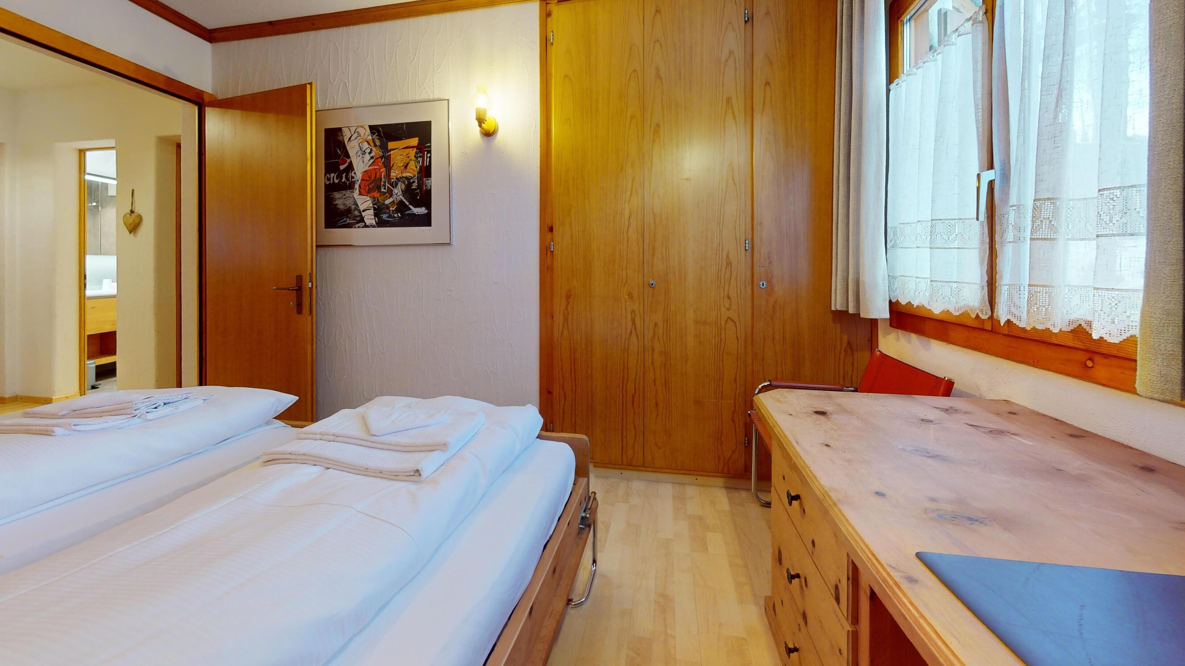 Een hotelkamer met twee bedden, een houten garderobe, een bureau en een raam met kantgordijnen.