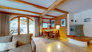 A cozy room with a wooden ceiling, a sofa with cushions, a dining table with chairs, and a fireplace. - 5½-roomed apartment on the ground floor, 140m2. (Celerina/Schlarigna)