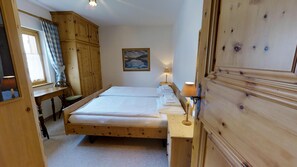 Une pièce avec deux lits en bois, un bureau, une chaise, une armoire et un tableau accroché au mur.