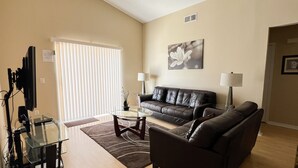 Ein Wohnzimmer mit braunem Ledersofa, einem Glastisch und einem Fernseher auf einem Standfuß.