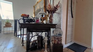 Une pièce avec un plancher en bois, un bureau avec une lampe, un miroir et un vase contenant des plantes séchées.