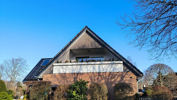 Une maison moderne dotée d’un toit en pente, de panneaux solaires et d’un balcon agrémenté de plantes.