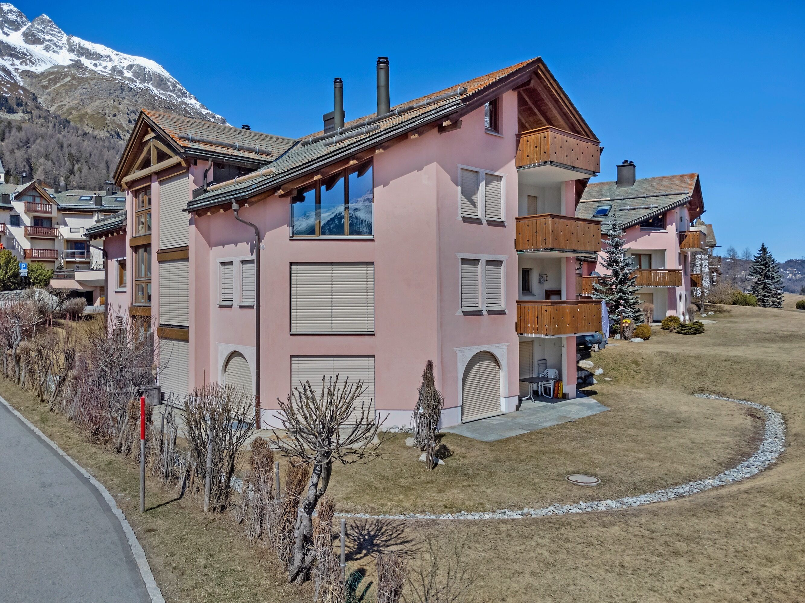 Un edificio rosa de varios pisos con balcones, un garaje y vistas a montañas nevadas.