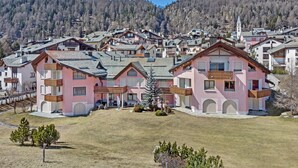 Eine Gruppe rosafarbener Gebäude mit Balkonen, umgeben von einer grünen Fläche und Bergen im Hintergrund.