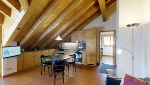 Eine geräumige Küche mit Holzbalken, einem Essbereich mit Stühlen und einem an der Wand montierten Fernseher.