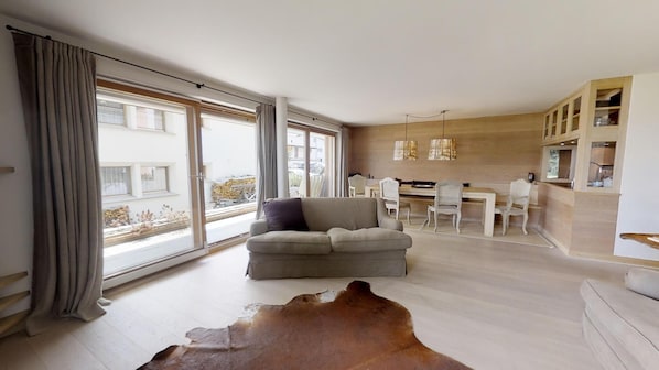 Ein modernes Wohnzimmer mit einer Couch, einem Esstisch, Stühlen und einer Küchenzeile mit Schränken.