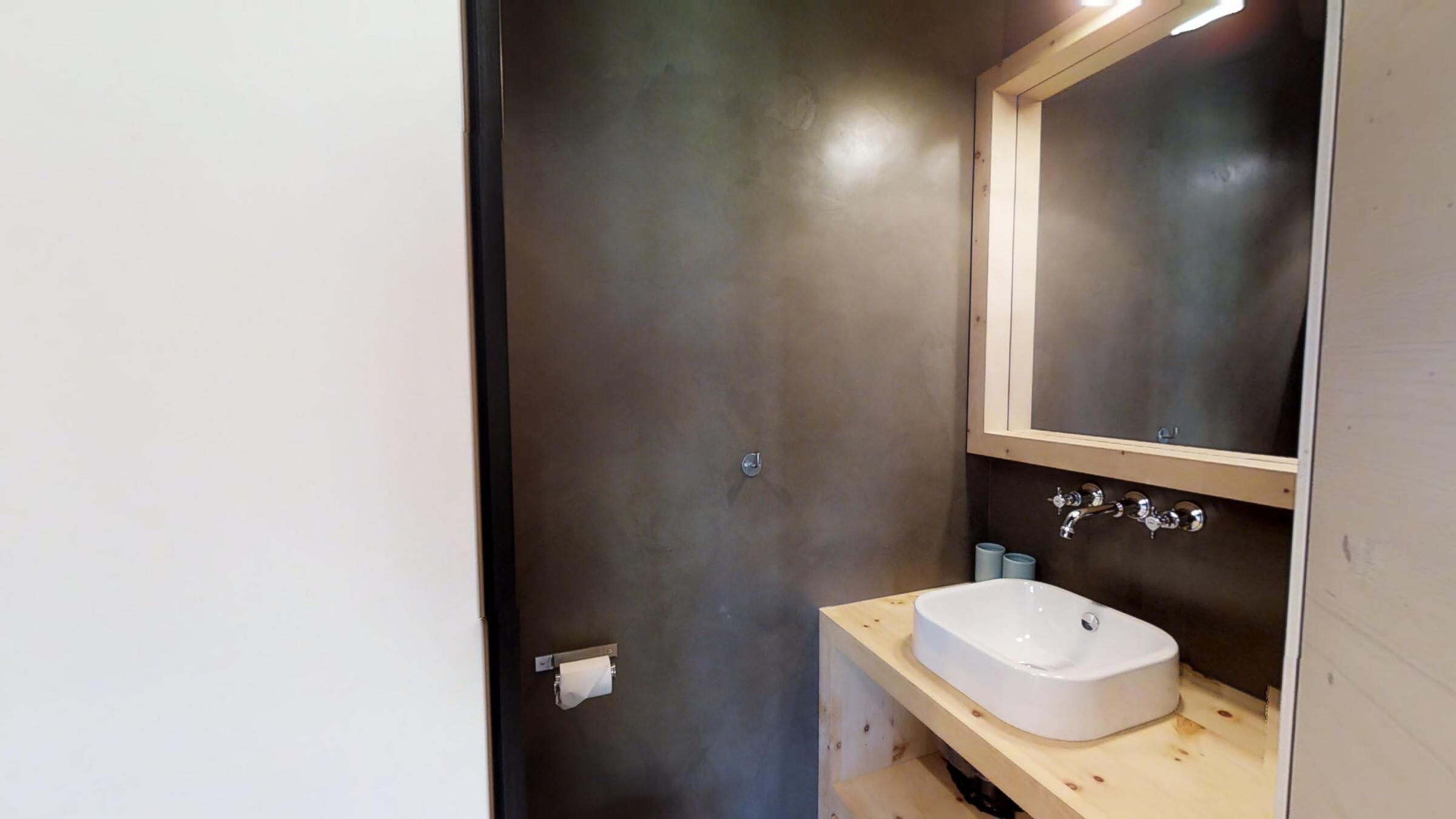 A small bathroom with a white sink, a mirror above it, and a dark wall.
