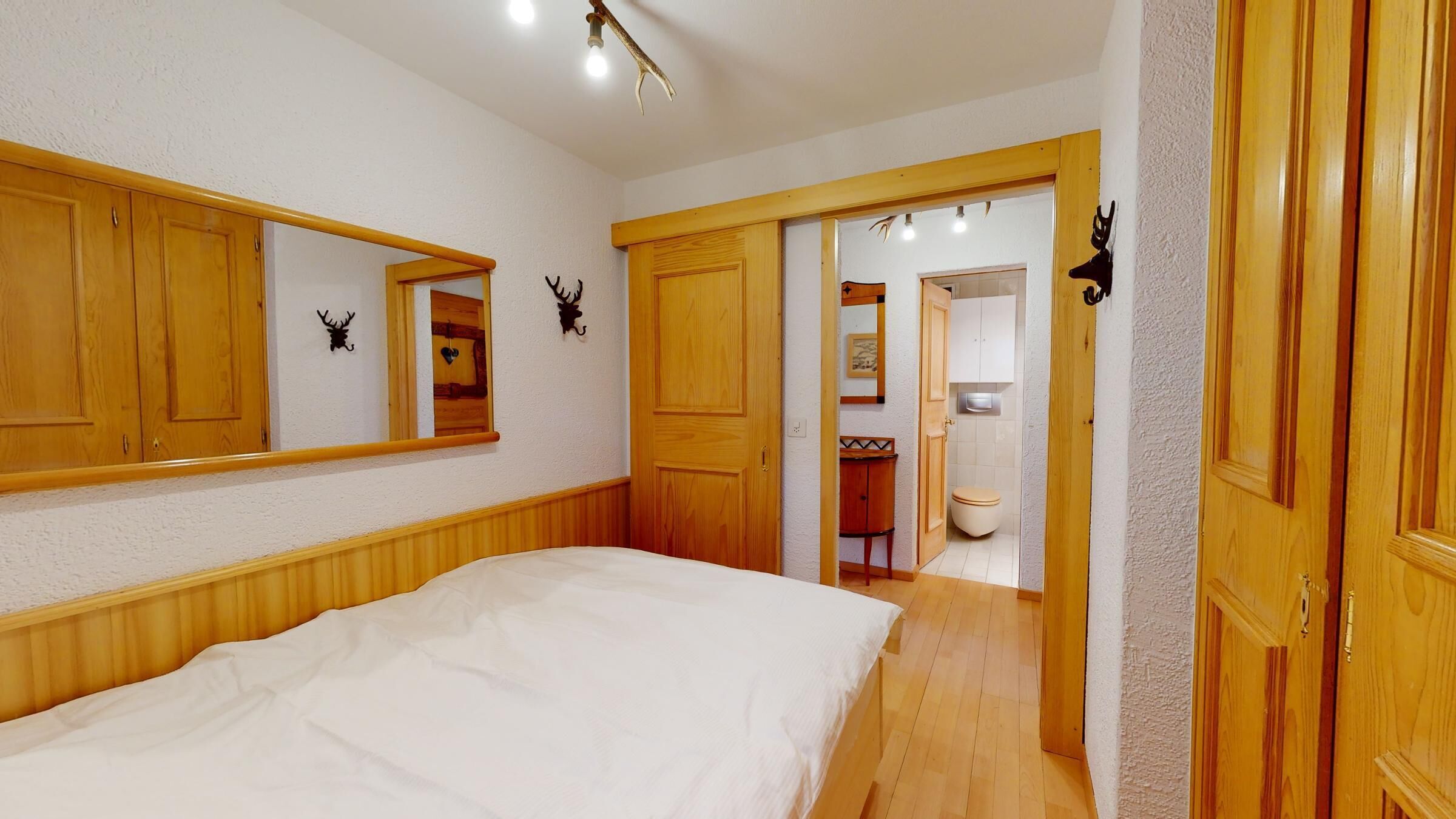 Ein Schlafzimmer mit Bett, Holzschrank und angrenzendem Badezimmer.