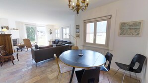 A spacious living area with a round table, comfortable seating, and large windows providing natural light. - 3 ½ -room apartment on the ground floor ca. (Silvaplana-Surlej)