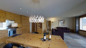 A modern kitchen with wooden cabinetry, a dining table with two wine bottles, and a contemporary pendant light.